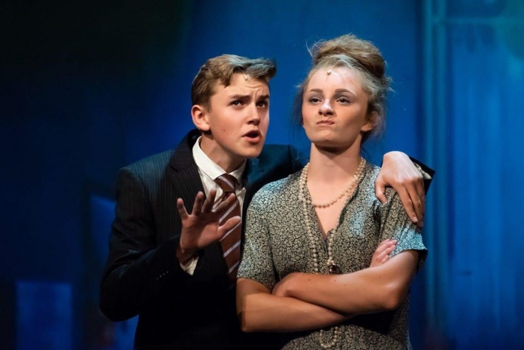 King's InterHigh pupil & musical actor, Daniel Wilmott, acting on stage wearing a suit & tie. His has his arm around a fellow actress.