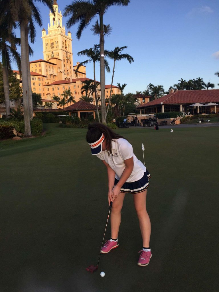 King's InterHigh pupil & golfer, Darcy Harry, practicing on a putting green, with palm trees and a grand building in the background.